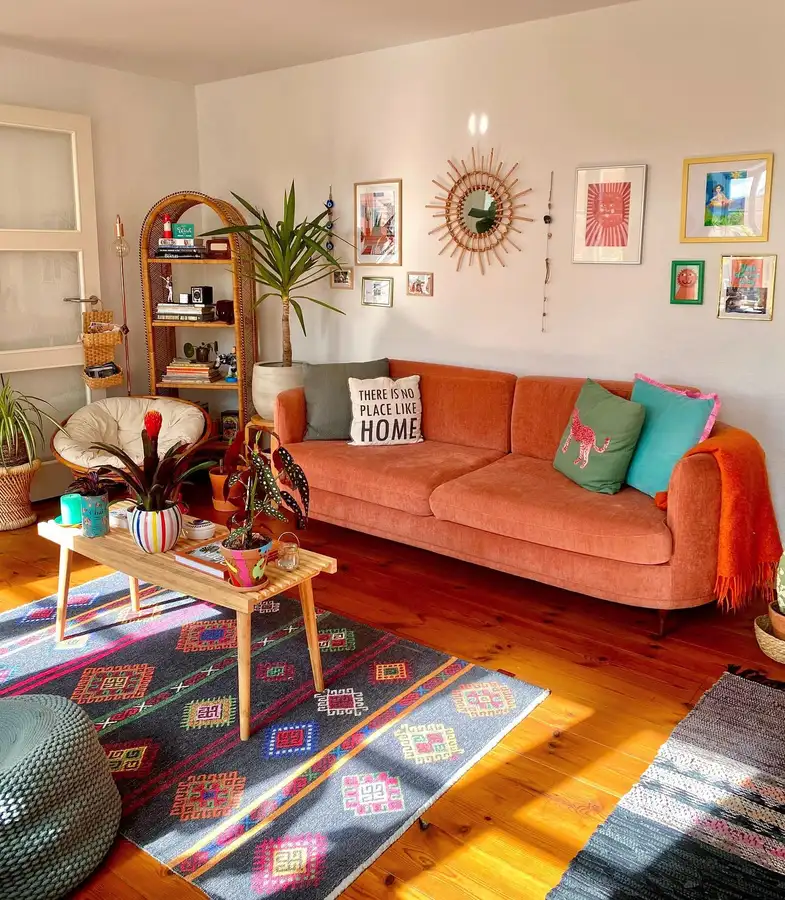 Bright living room with burnt orange sofa, multicolor patterned rug, colorful cushions, plants, and wall art