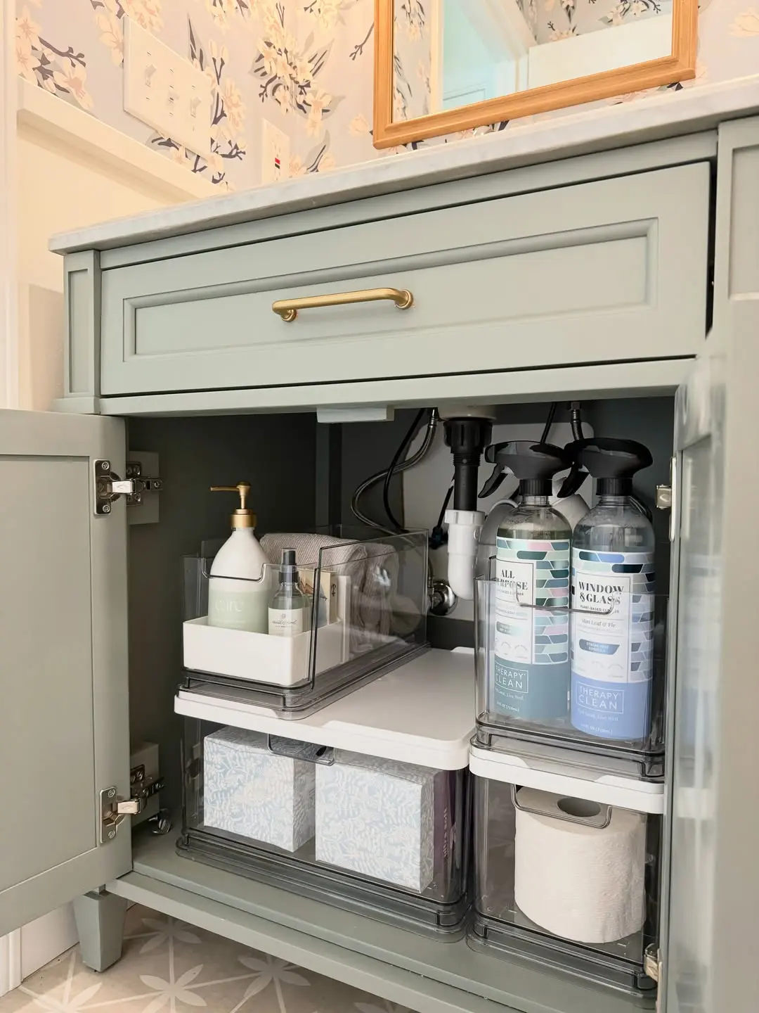 Under sink bathroom cabinet with clear pull-out organizers arranged around exposed plumbing and cleaning supplies