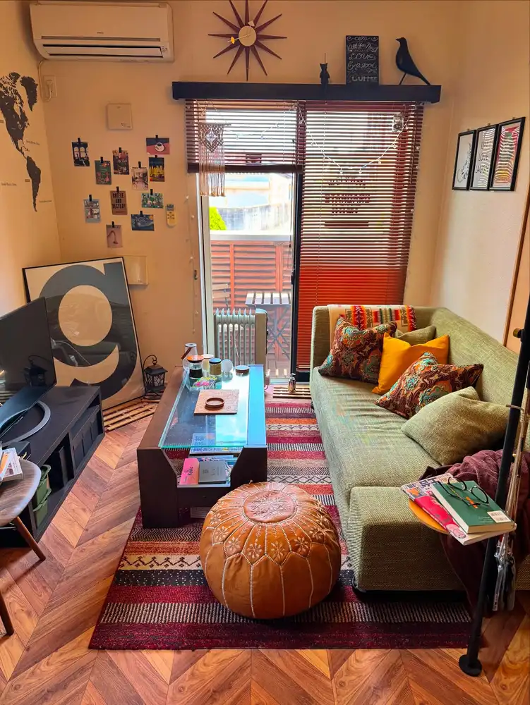 Narrow living room with a long patterned rug, coffee table, pouf, sofa, and warm colorful accents.