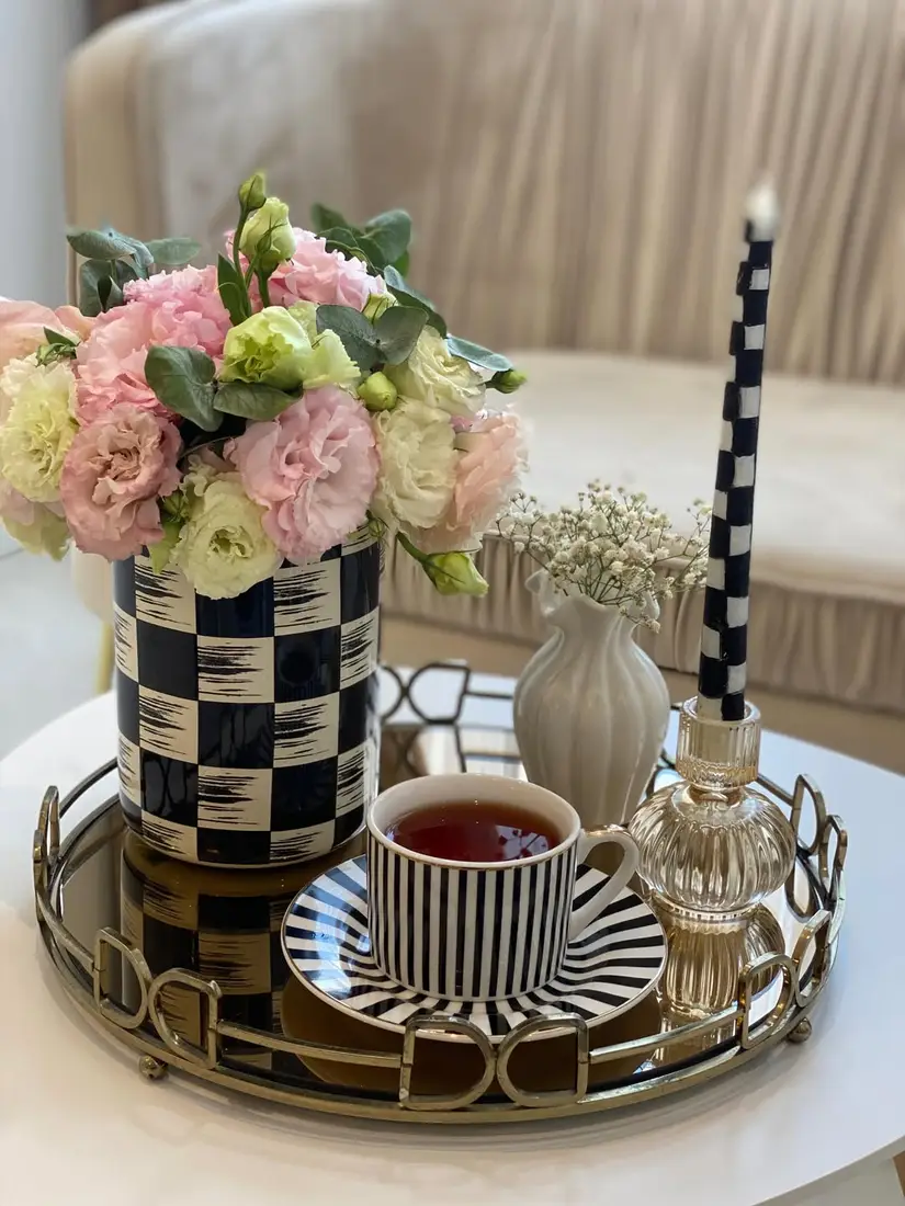 Mirrored coffee table tray with checkerboard vase, striped cup, pink flowers, and glass candleholder