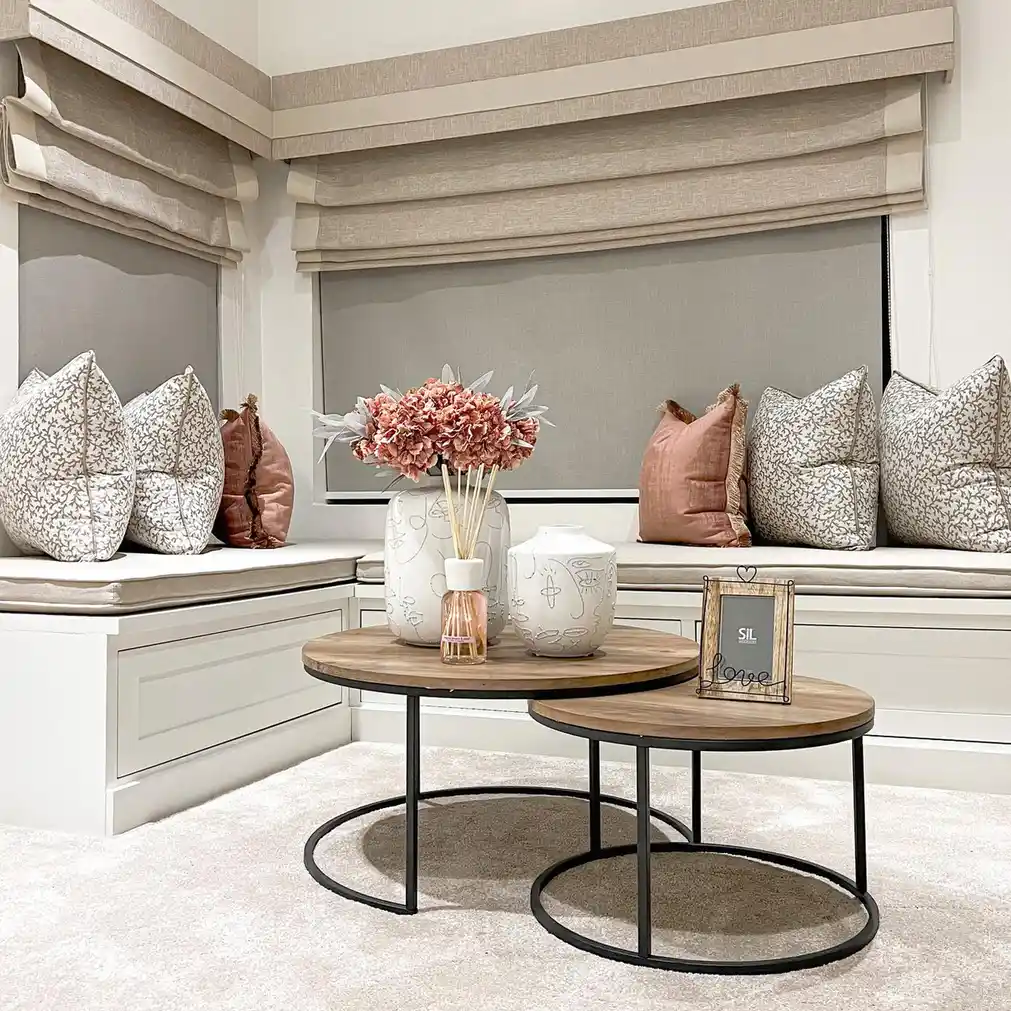 Bright living room corner with built-in window benches, patterned cushions, and round nesting coffee tables