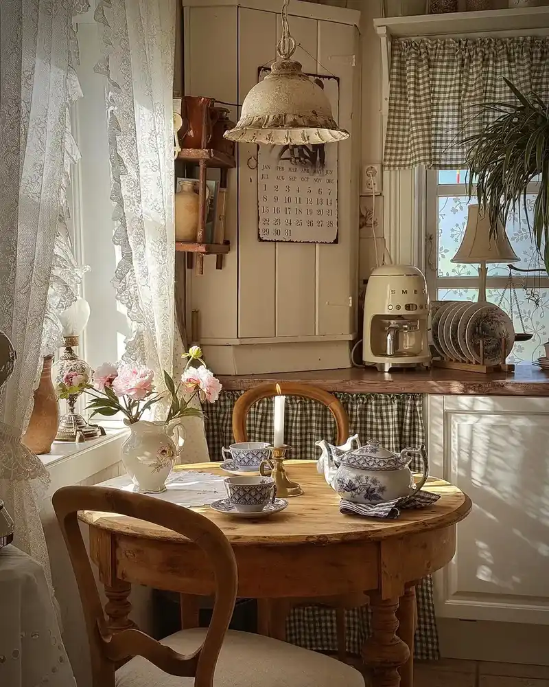 Cozy vintage kitchen with lace curtains, gingham fabric, blue and white dishes, and wood table