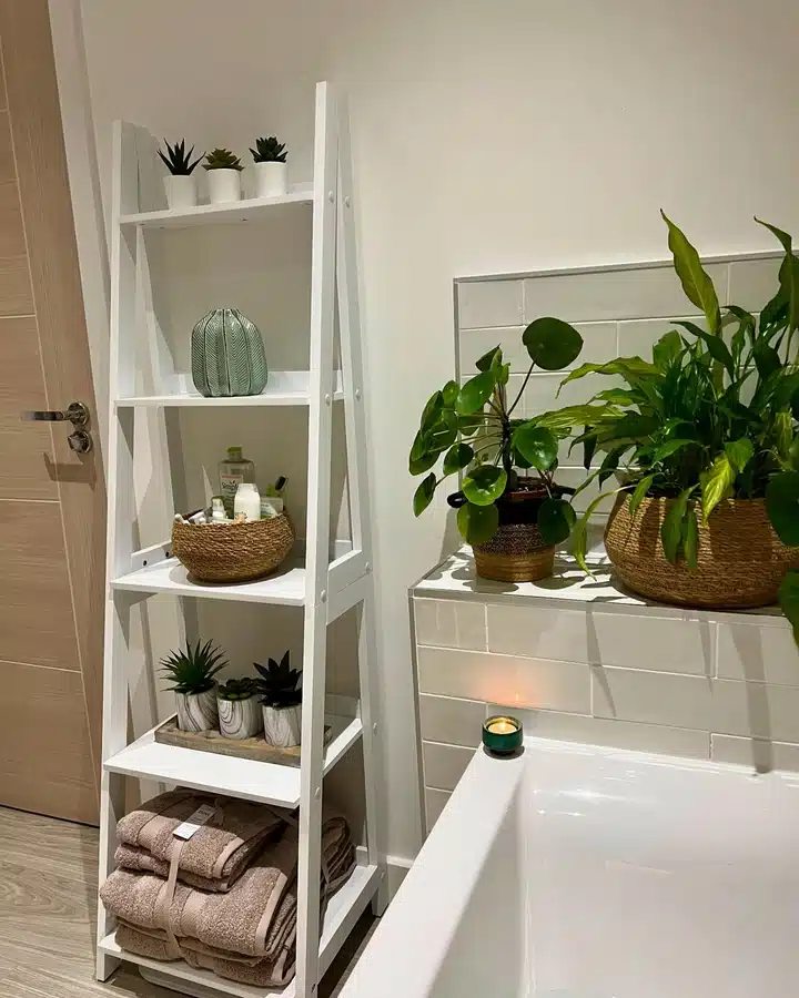 04 Leaning ladder shelf in a small bathroom holding folded towels, baskets, plants, and decor