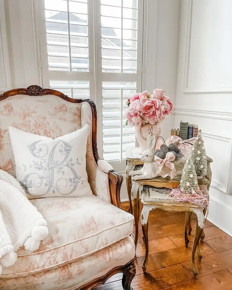 Vintage living room corner with carved armchair, rustic side tables, pink flowers, and soft neutral decor