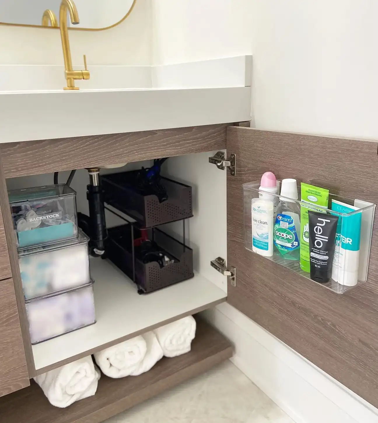 Bathroom vanity cabinet with clear door organizer, stacked drawers, pull-out baskets, toiletries, and rolled towels