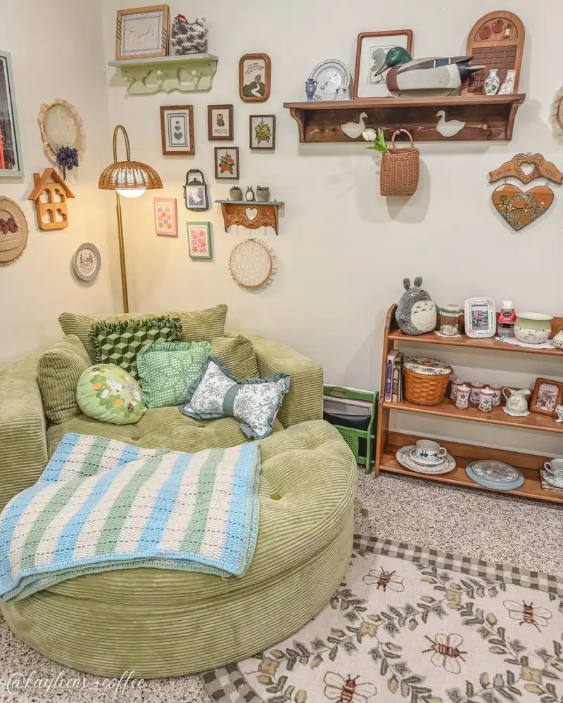 Cozy reading corner with an oversized green chair, crochet throw, patterned cushions, wall art, and a floor lamp.
