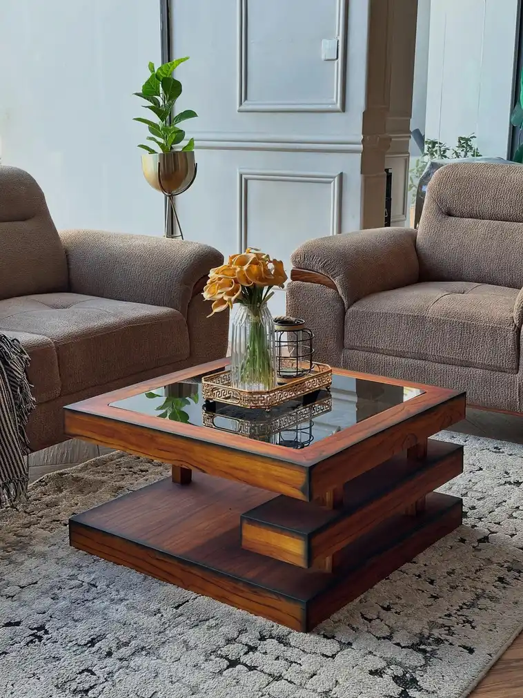 Square wood and glass coffee table styled with a small tray, orange flowers, and decorative accents