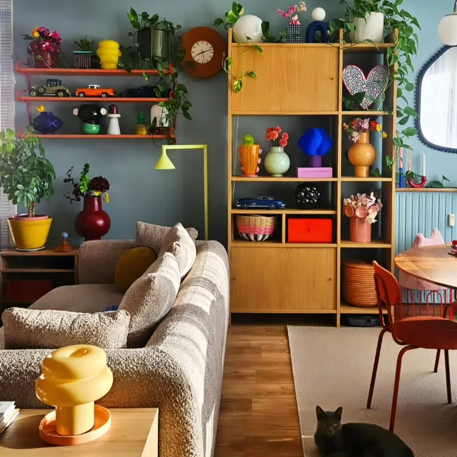 Colorful living room with neutral sofa, bright shelving decor, colorful lamps, plants, flowers, and accent chairs
