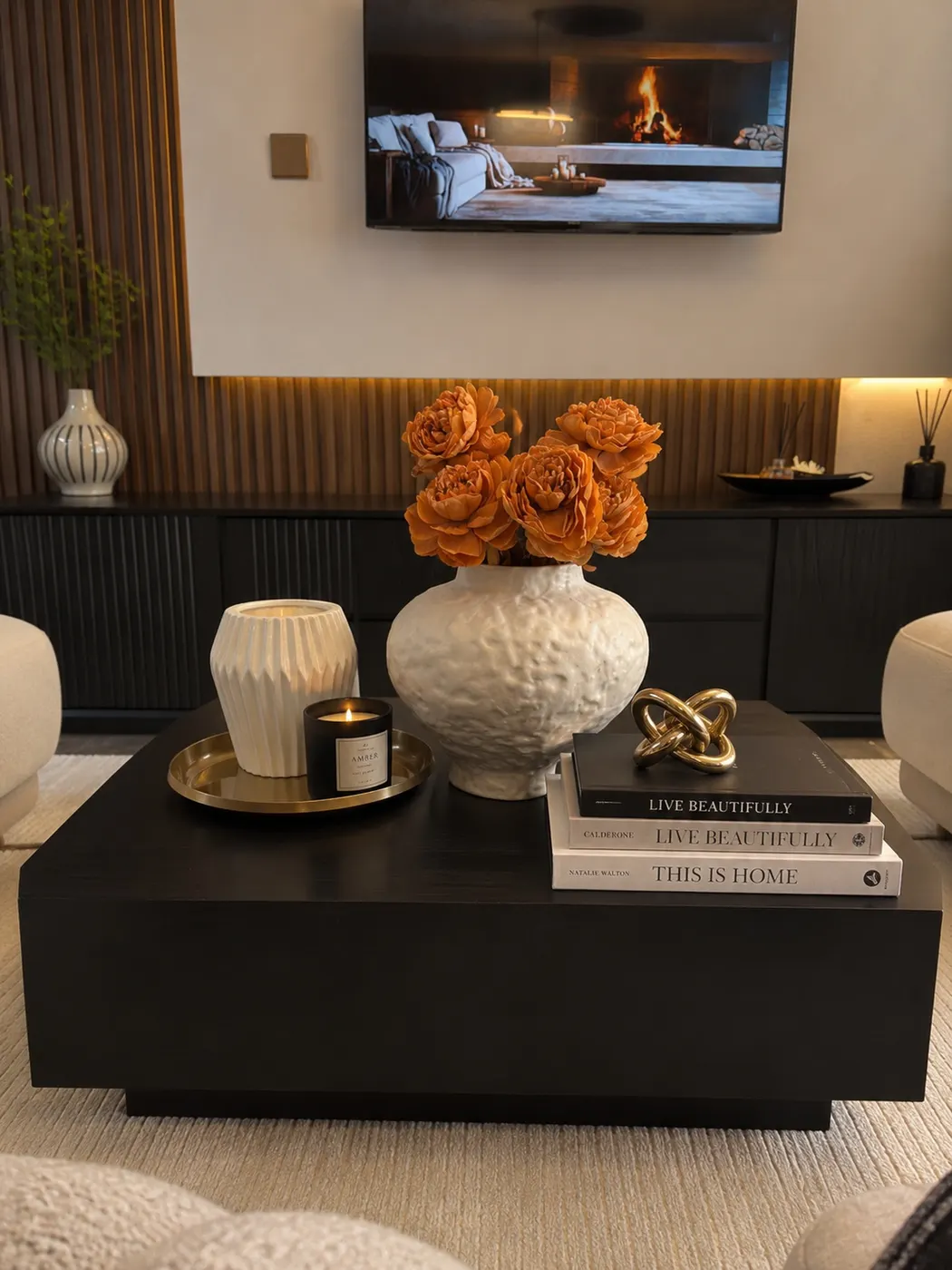 Large black coffee table with cream flower vase, books, gold knot decor, candle, and small tray
