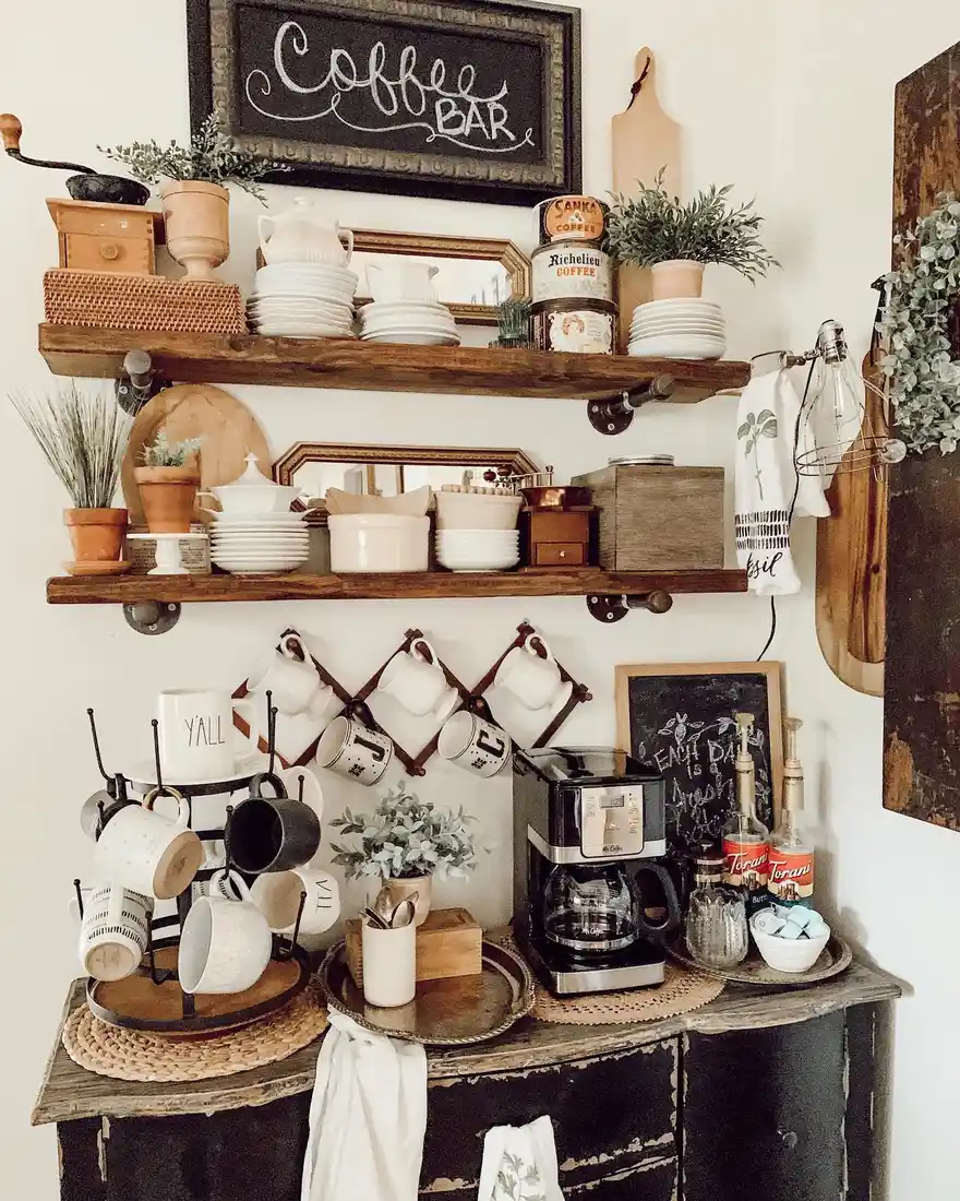 Rustic farmhouse coffee station with distressed cabinet, wooden shelves, mug racks, vintage tins, plants, and coffee machine