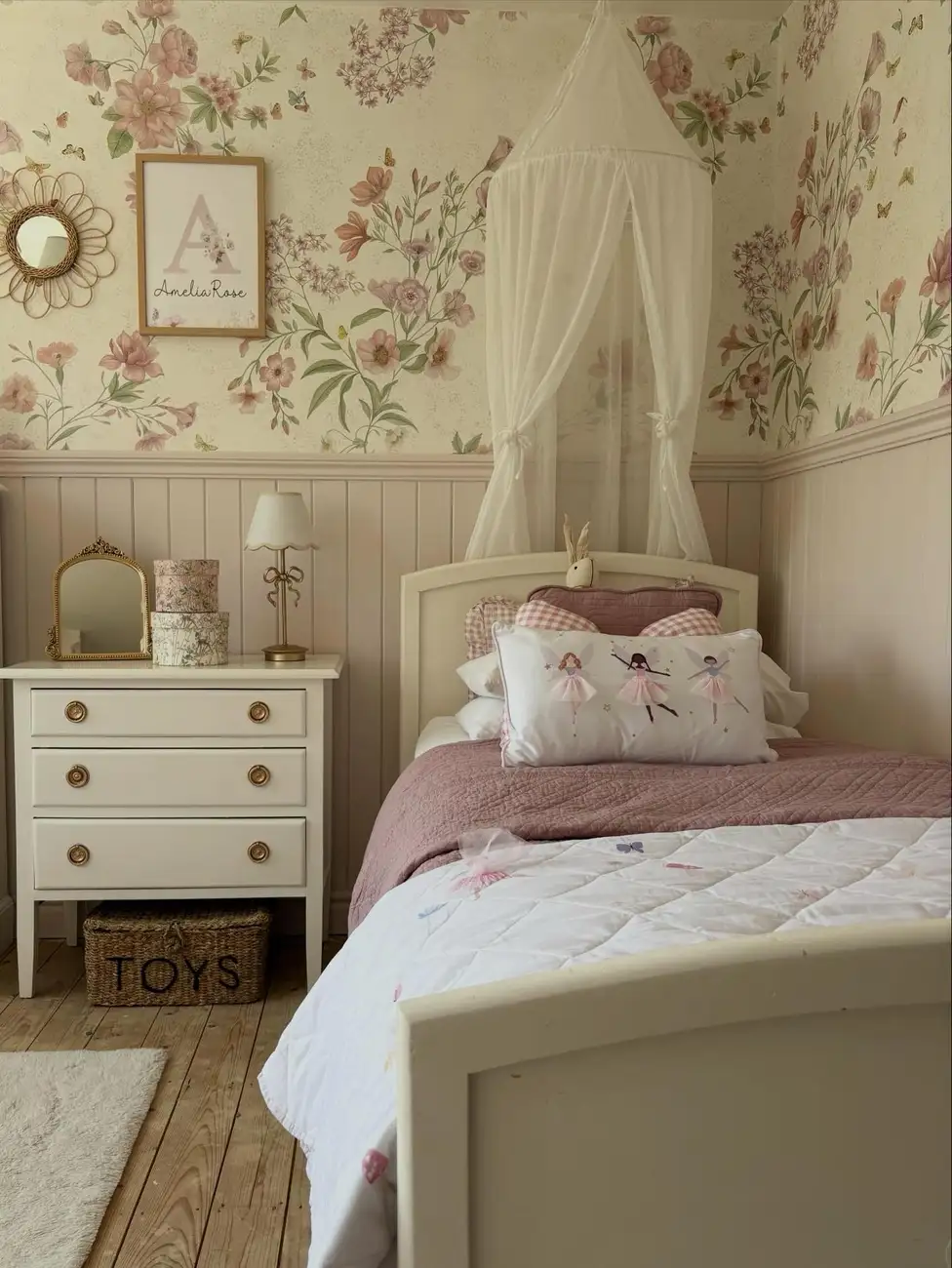 Girls bedroom with floral wallpaper, beige wall paneling, white canopy, and dusty pink bedding