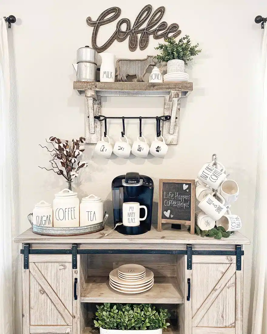 Rustic farmhouse coffee bar with weathered wood cabinet, black metal hardware, hanging mugs, canisters, shelves, and coffee maker