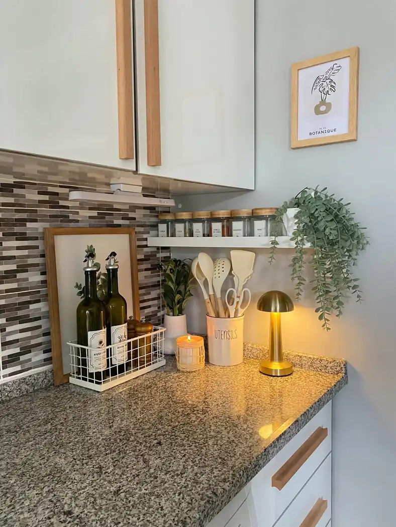 Granite kitchen counter organized with oil bottles in a wire basket, spice shelf, utensils and trailing greenery