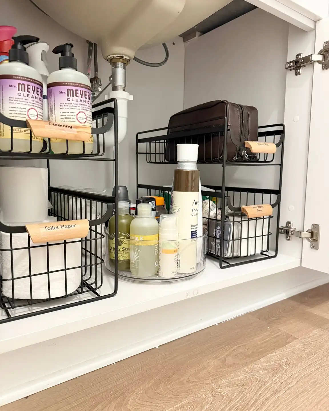 Under sink bathroom cabinet with a clear turntable between two tiered storage racks filled with bathroom supplies