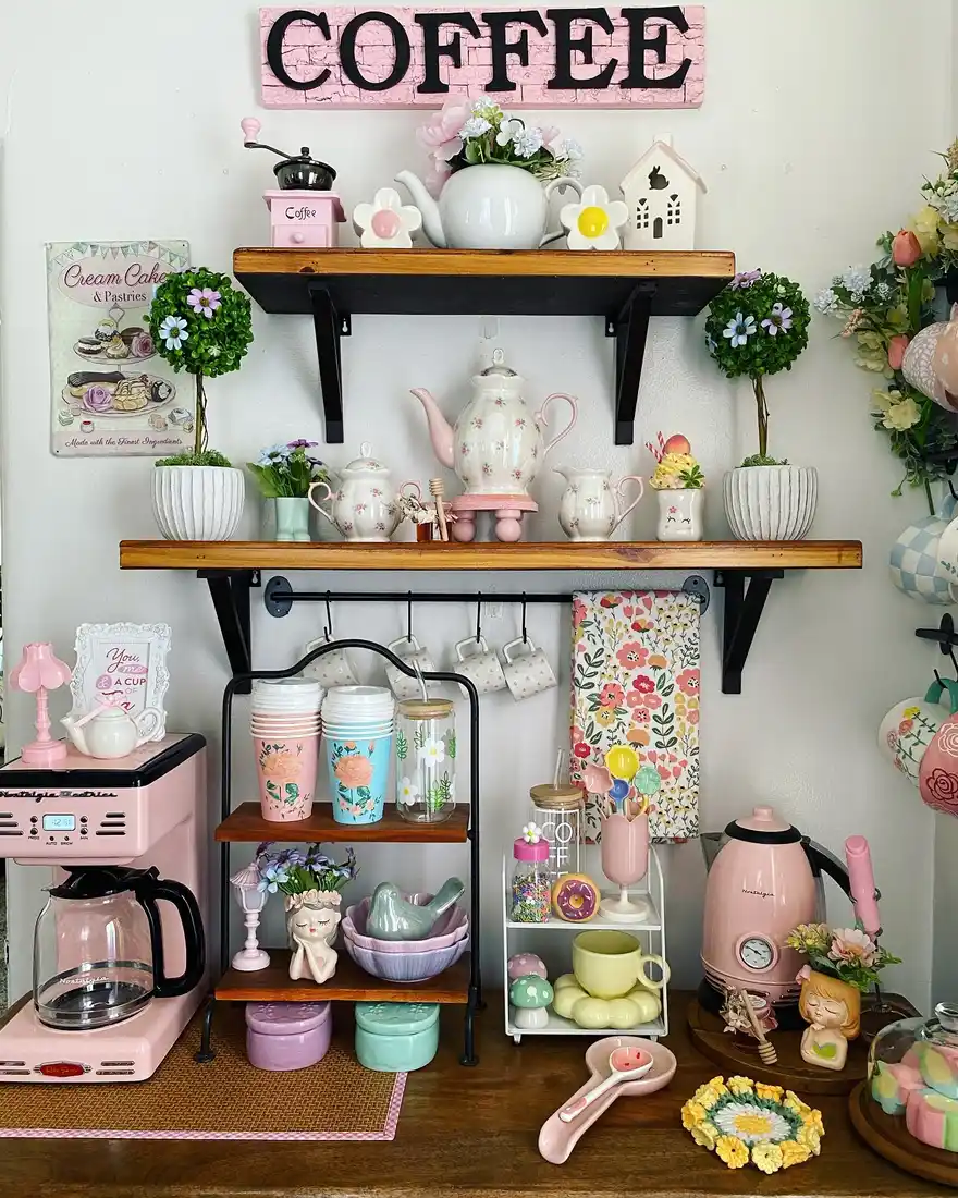 Pastel coffee station with pink appliances, floral mugs, mint and lilac accessories, shelves, and flower decor