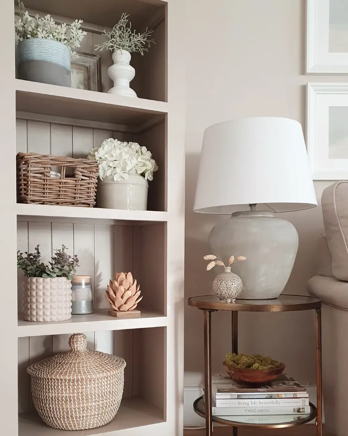 Neutral living room corner with built-in shelves, woven baskets, ceramic decor, flowers, and large table lamp