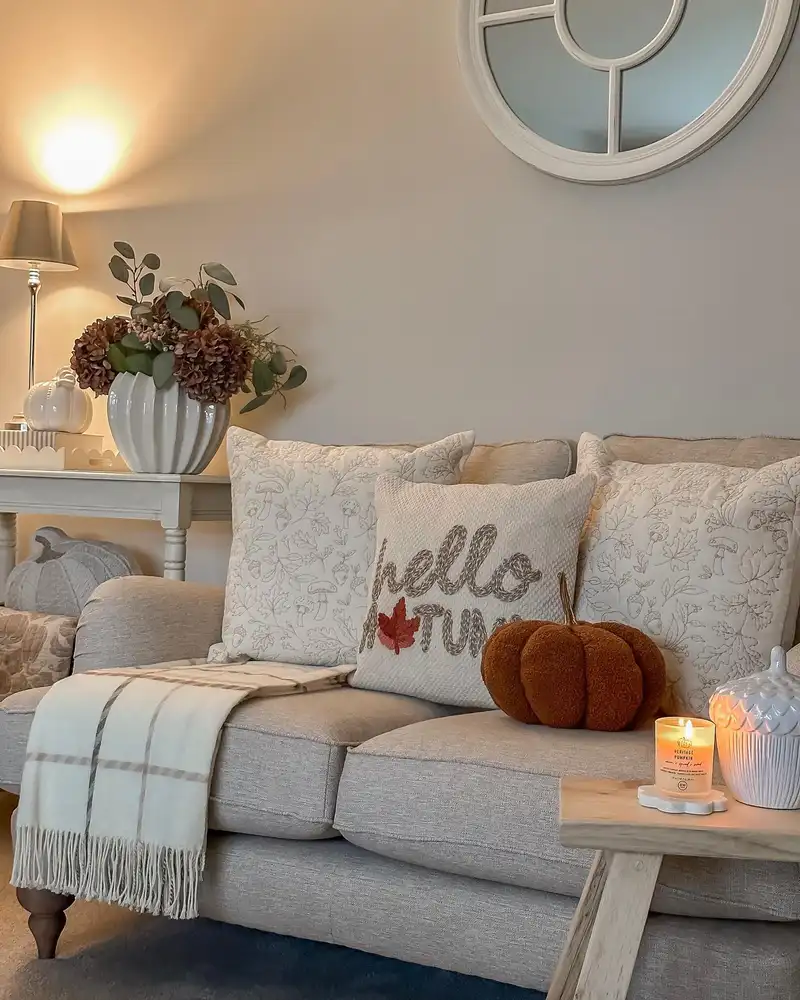 Neutral small living room decorated for fall with a rust pumpkin, warm candlelight, brown florals, and cozy textiles.