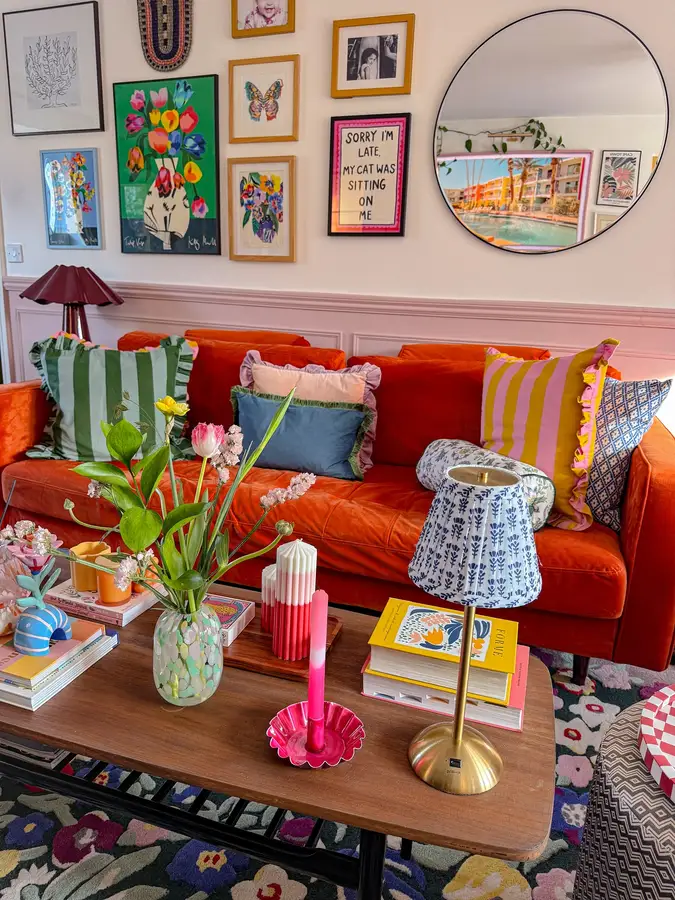 Colorful living room with burnt orange sofa, pink paneled wall, mixed patterned cushions, floral rug, and warm decor