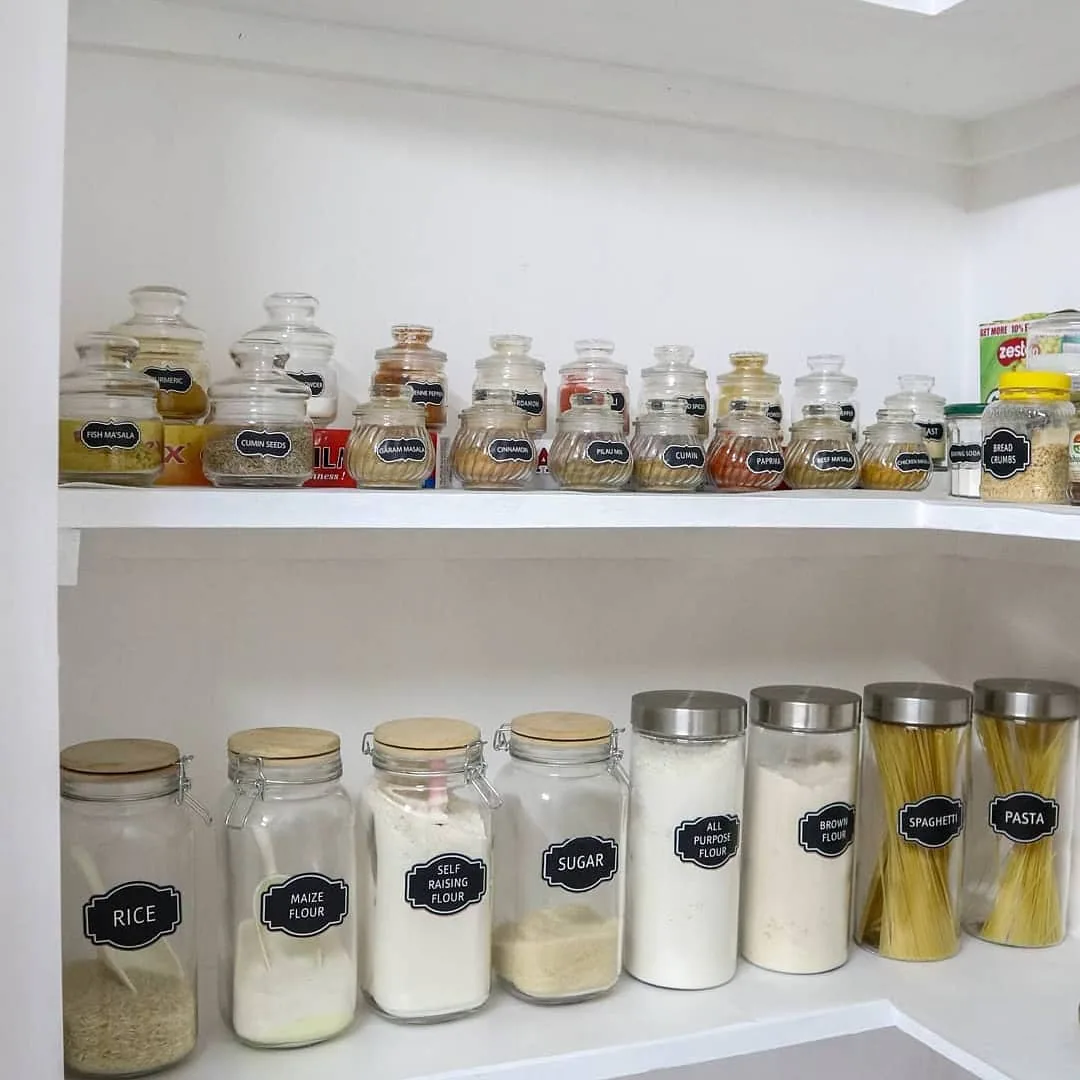 Small spice jars organized on a dedicated pantry shelf above clear containers filled with rice, flour, sugar, and pasta