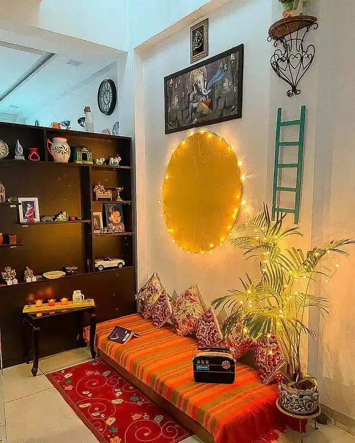 Warm lounge corner with low daybed, patterned cushions, tall plant, string lights, and large round wall decor