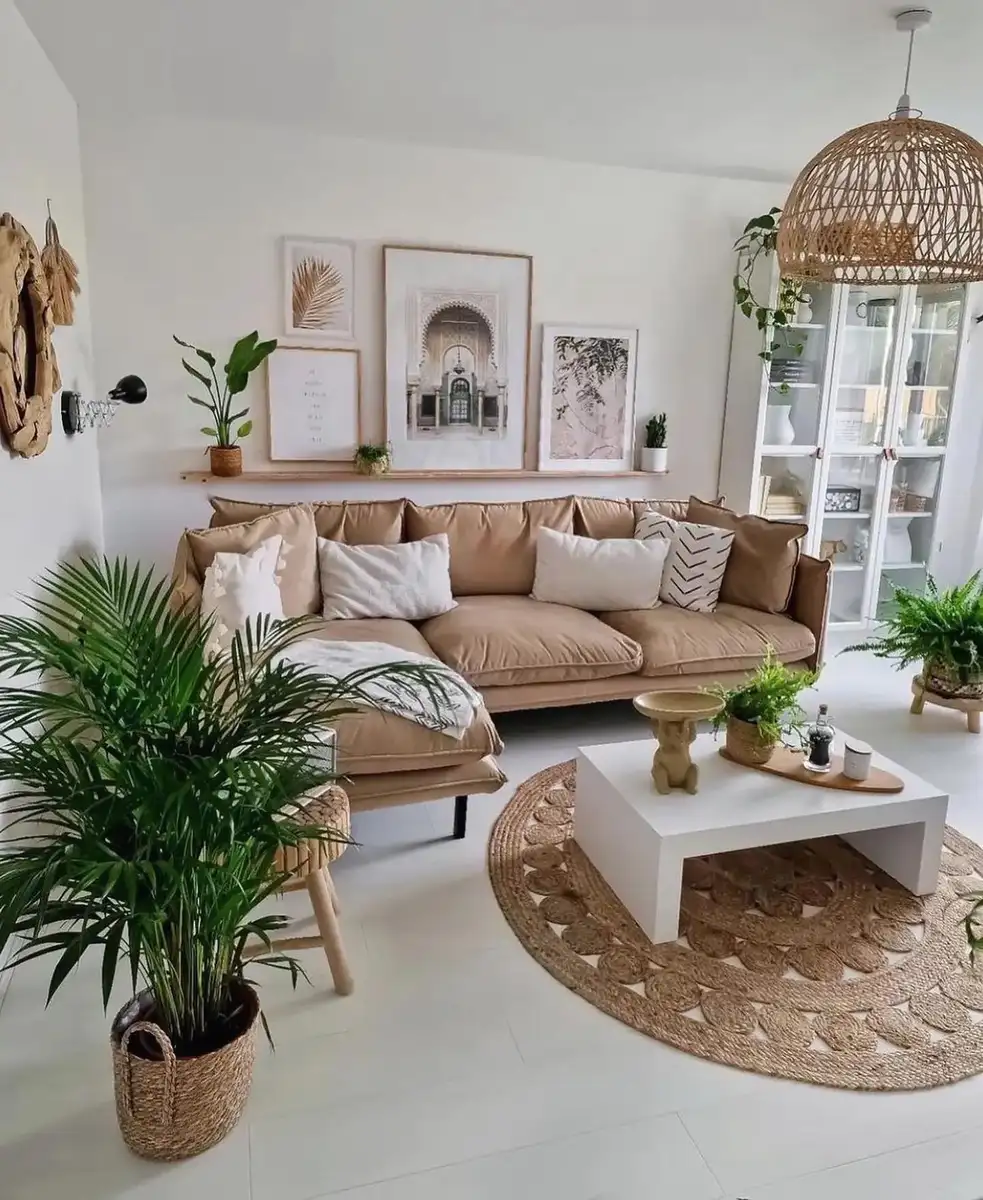 Bright neutral living room with a tan sectional, round jute rug, white coffee table, and several large leafy houseplants.