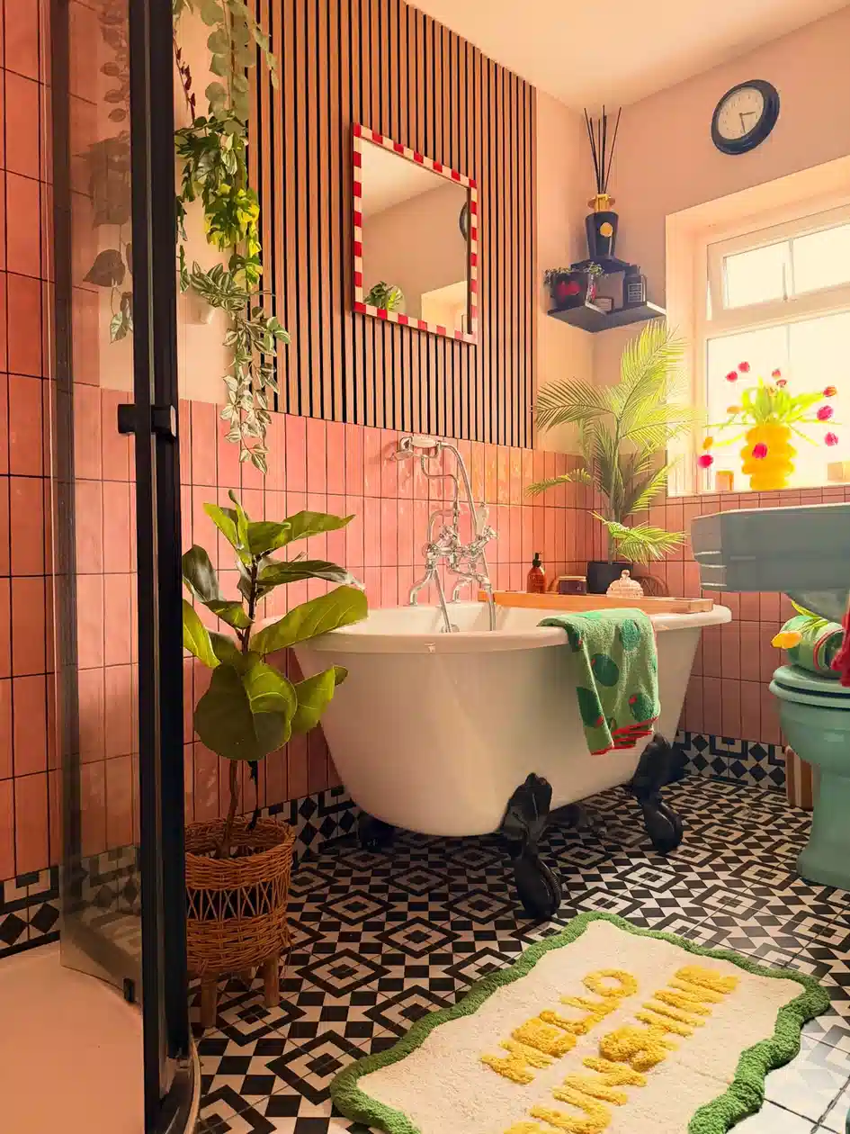 Pink bathroom with black and white patterned floor, freestanding tub, striped mirror, and green plants