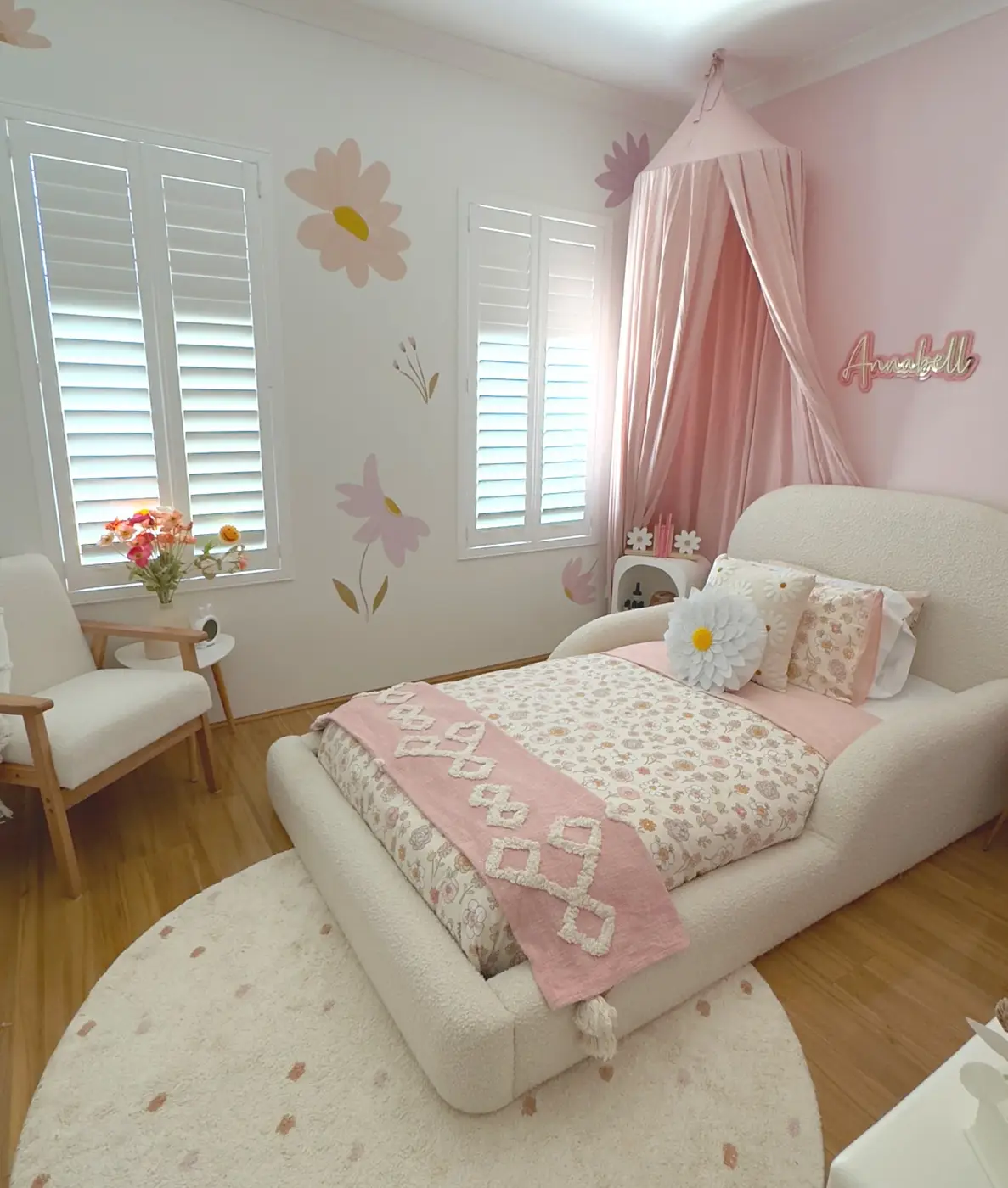 White girls bedroom with oversized daisy wall decorations, pink canopy, and textured white bedding