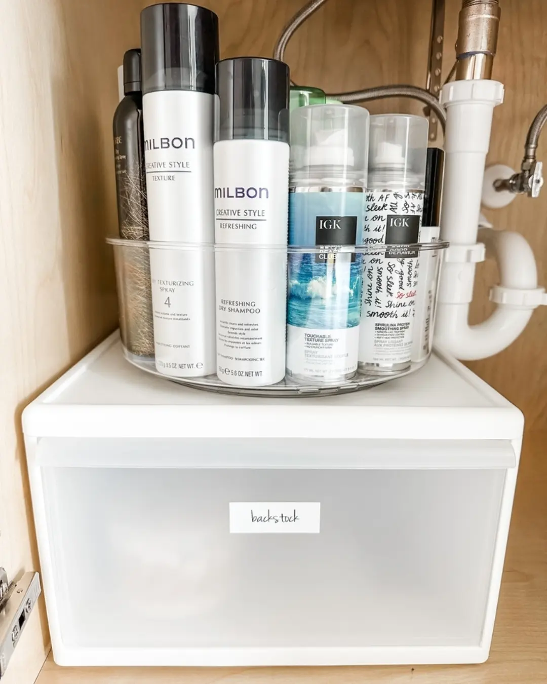Under sink bathroom storage with a frosted drawer topped by a clear turntable holding tall hair care bottles