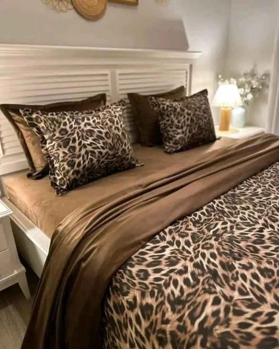 Leopard print bedding layered with chocolate brown sheets and a white upholstered headboard