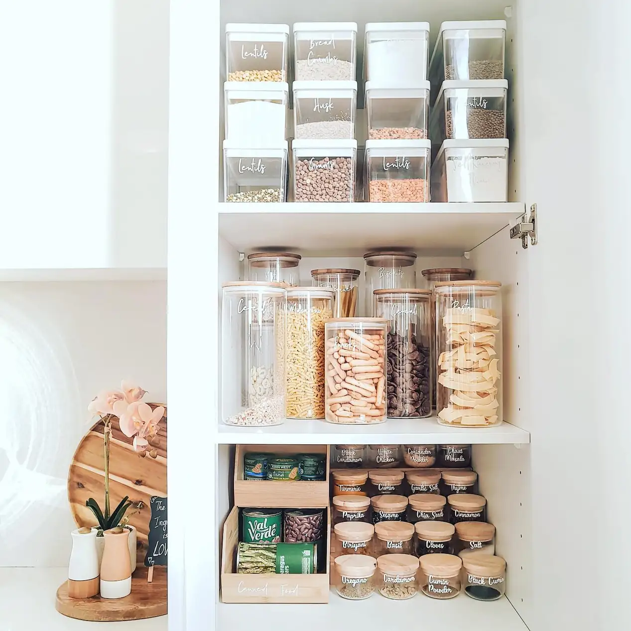 Pantry shelves organized with different container heights including stacked bins, tall dry food jars, and small spice containers