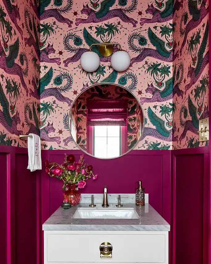 Bold pink bathroom with deep magenta paneling, patterned wallpaper, white vanity, and round mirror