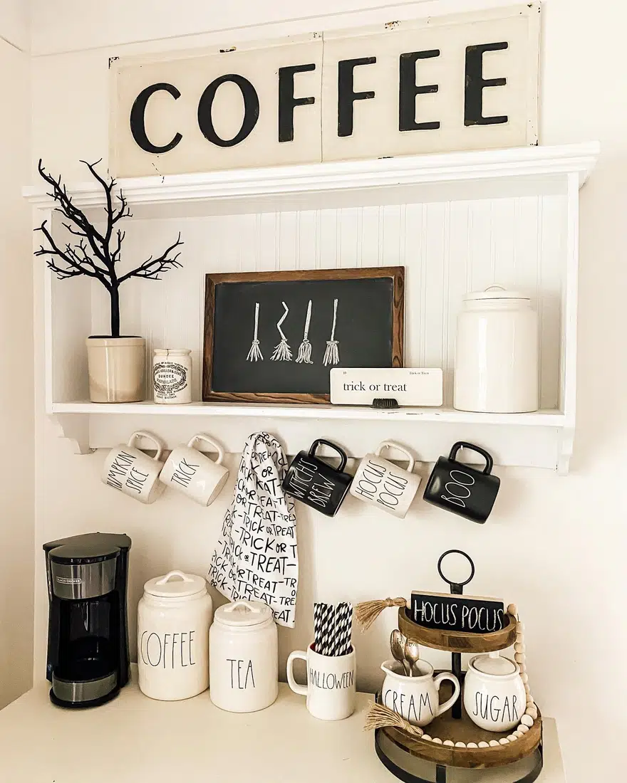 Halloween farmhouse coffee bar with seasonal mugs, black and white signs, cream canisters, tiered tray, branches, and coffee maker