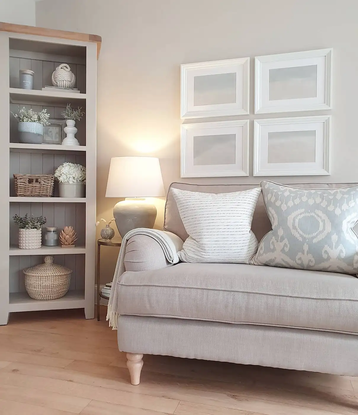Neutral living room corner with pale sofa, built-in shelving, side table, and glowing ceramic lamp
