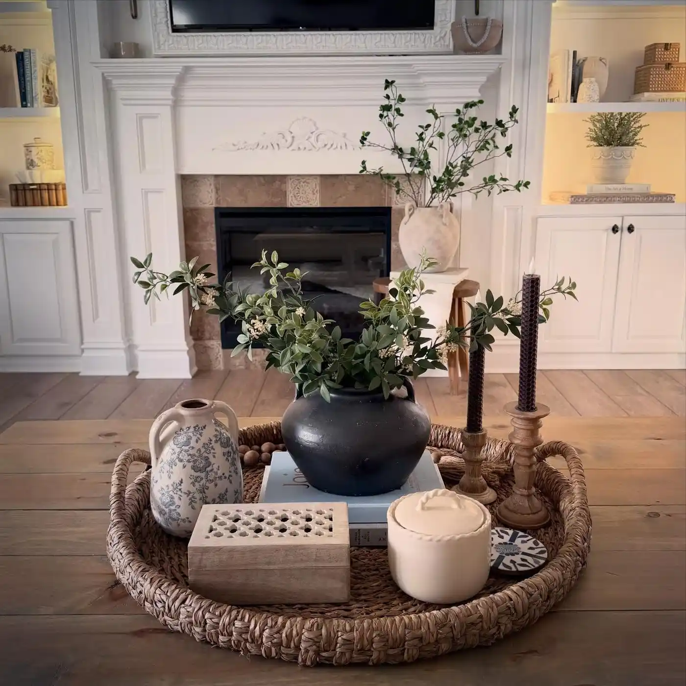 Wood coffee table with large woven tray, black vase, greenery, books, candles, and pottery