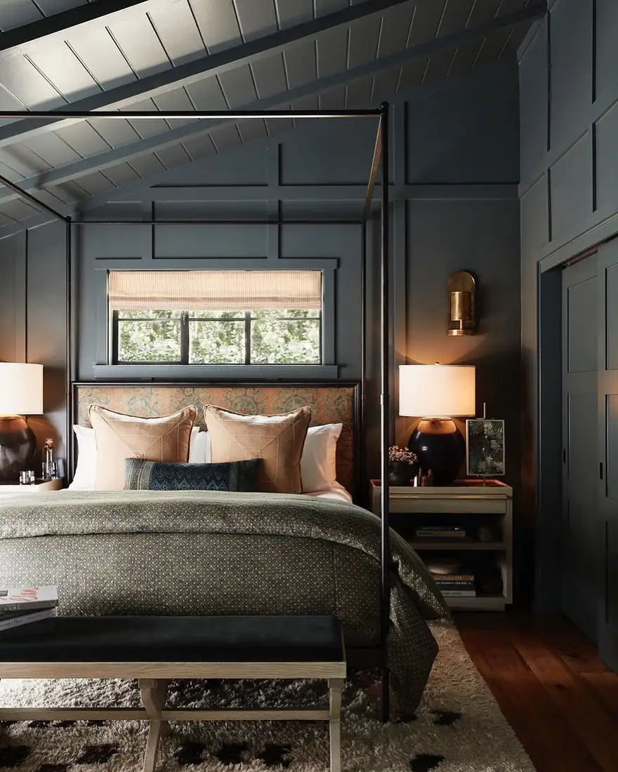 Dark blue attic bedroom with canopy bed, paneled walls and warm bedside lamps