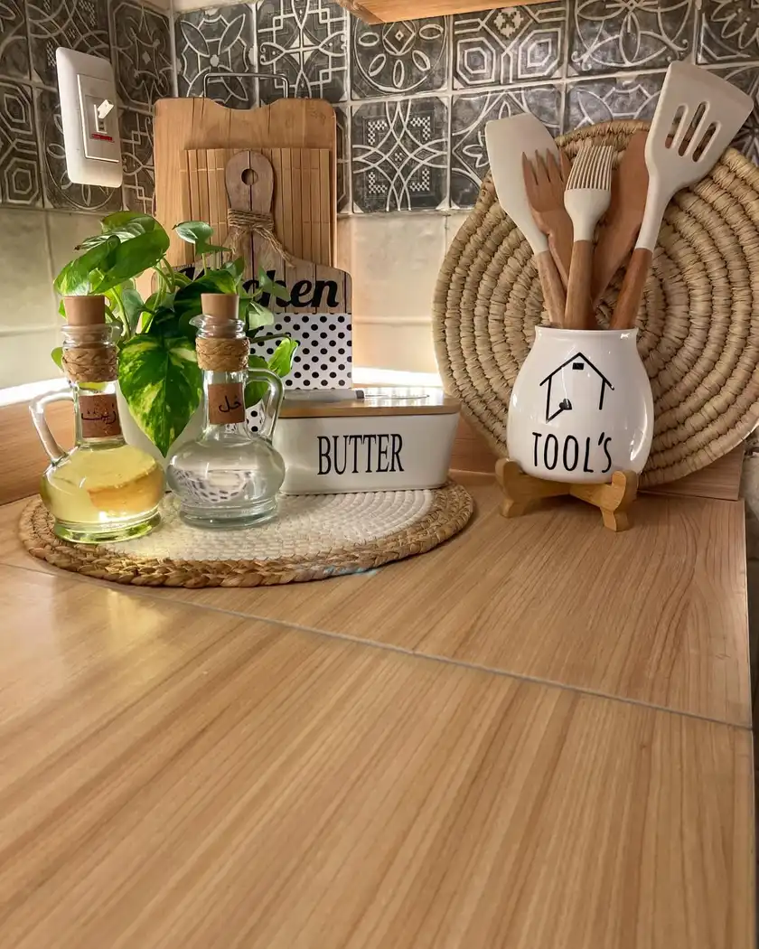 Warm wood kitchen counter styling with oil bottles, butter dish, utensils, cutting boards and green plant