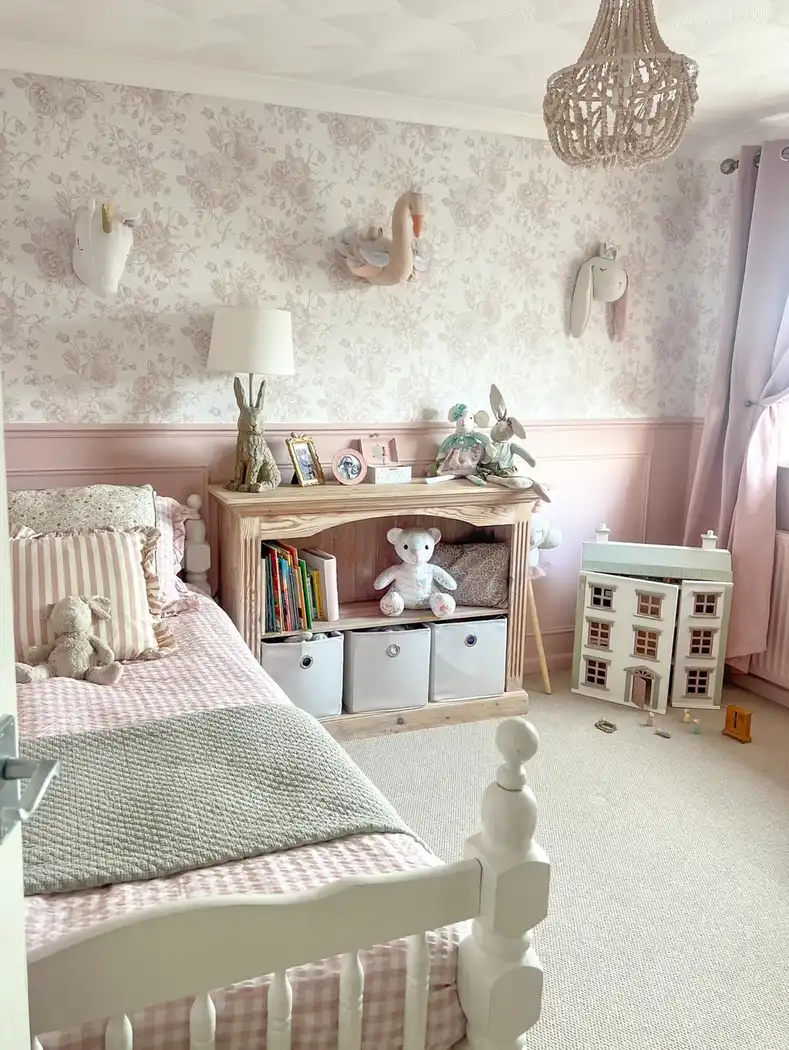 Girls bedroom play corner with wooden toy shelf, baskets, dollhouse, floral wallpaper, and pink paneling