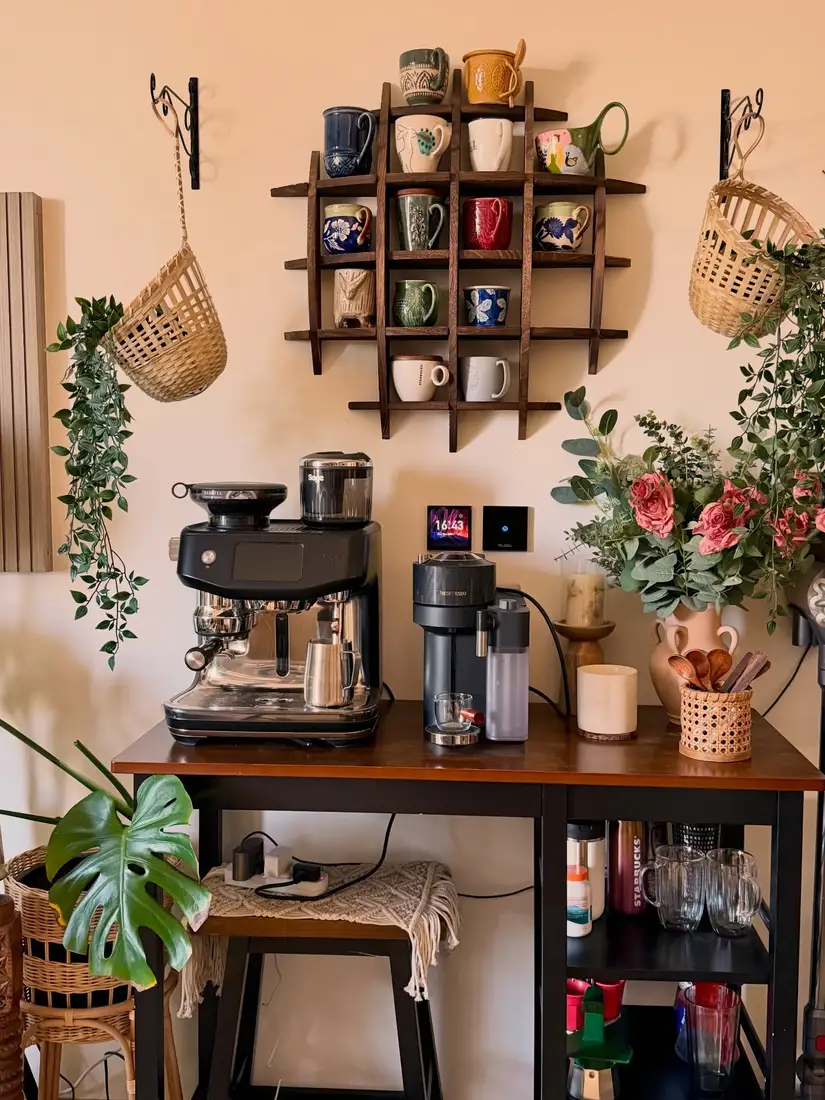 Coffee station with wooden wall mug rack, black espresso machine, colorful mugs, plants, flowers, and dark wood counter