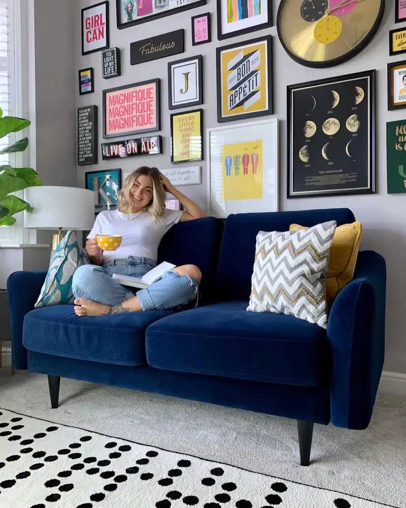 Blue sofa beneath a colorful gallery wall with black frames and bright yellow accent cushions.