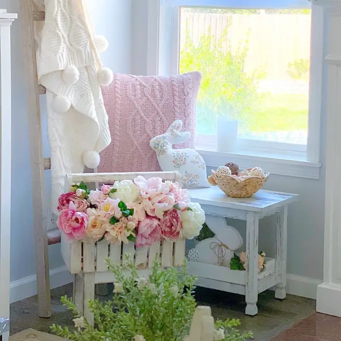Soft pastel corner with rustic table, pink flowers, knitted blanket, decorative ladder, and seasonal accents