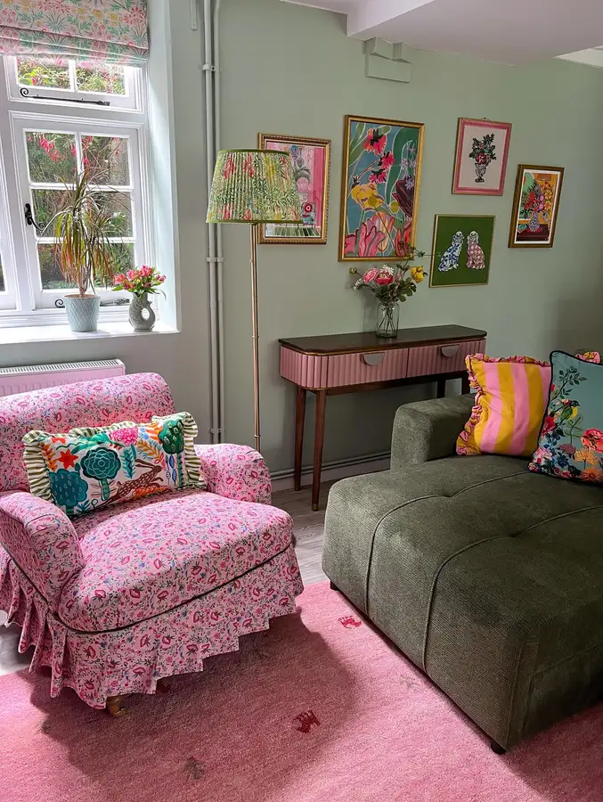 Colorful living room with olive green sofa, pink floral armchair, sage wall, pink rug, botanical art, and patterned cushions