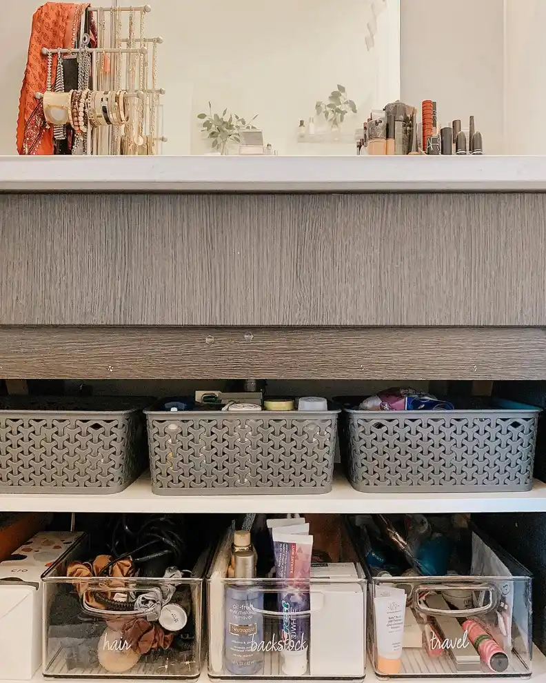 Bathroom vanity cabinet organized with patterned baskets and clear bins separating hair products, toiletries, and backups