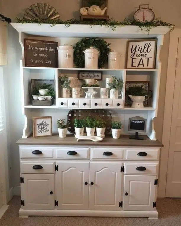 White farmhouse coffee hutch with cubby storage, mugs, small plants, jars, wood accents, and coffee machine