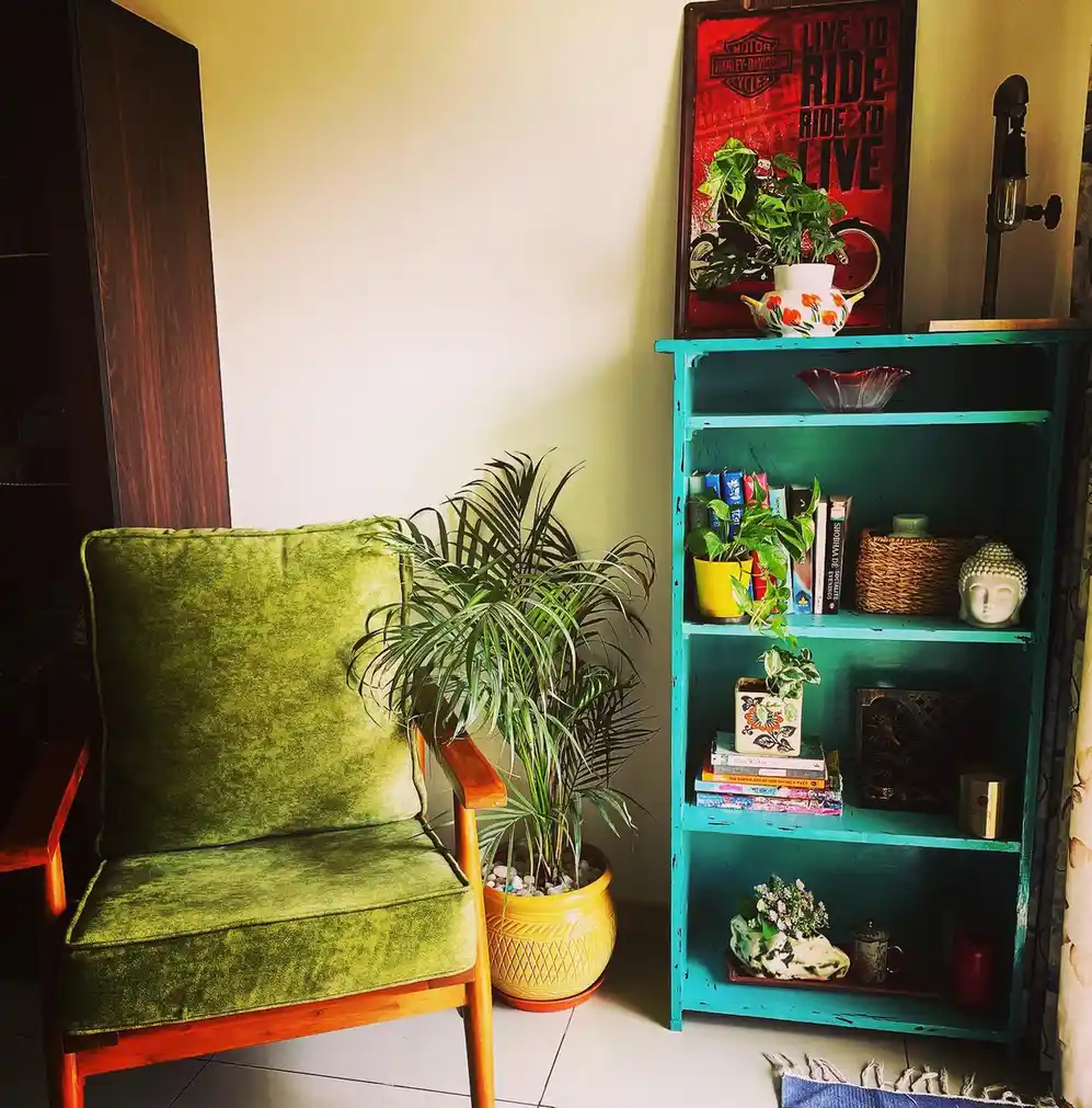 Colorful living room corner with olive green chair, turquoise bookcase, potted palm, books, and decorative objects