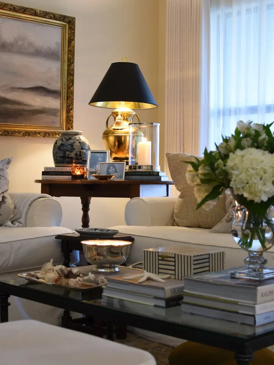 Dark wood side table styled with a brass lamp, blue-and-white jar, framed photos, stacked books, and candles.