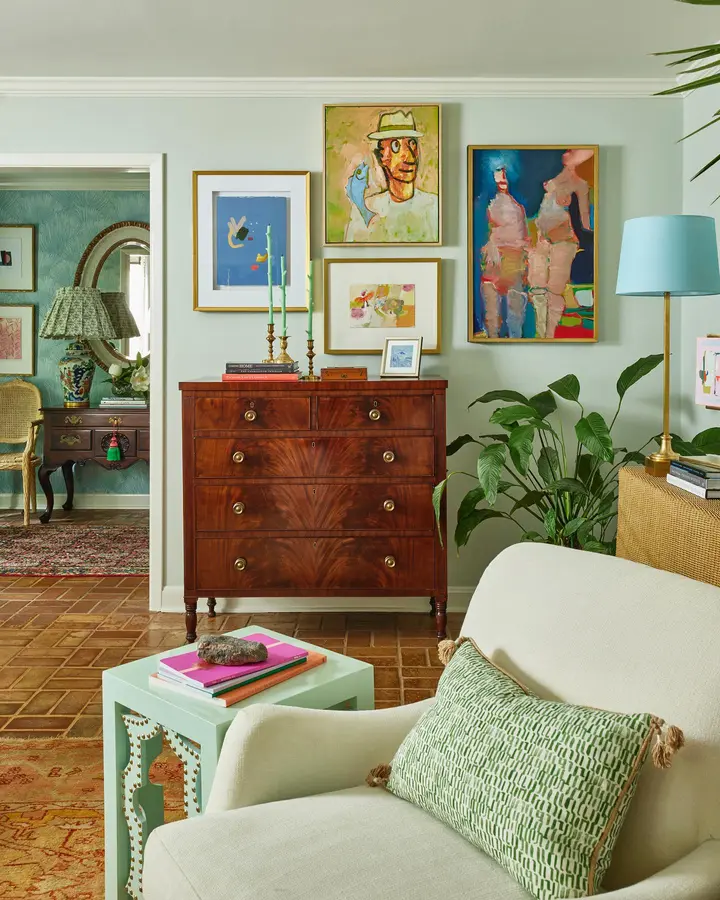 Soft green living room with cream chair, colorful gallery wall, mint side table, blue lampshade, and bright cushions