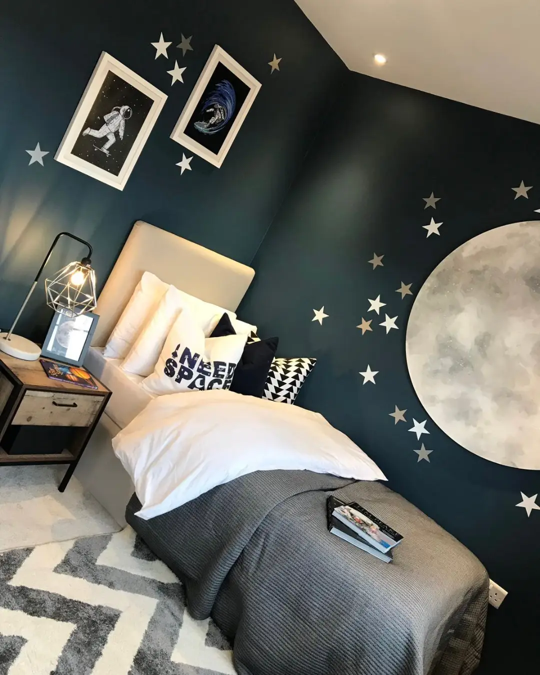 Dark blue bedroom wall with large moon, scattered stars, and simple gray and white bedding
