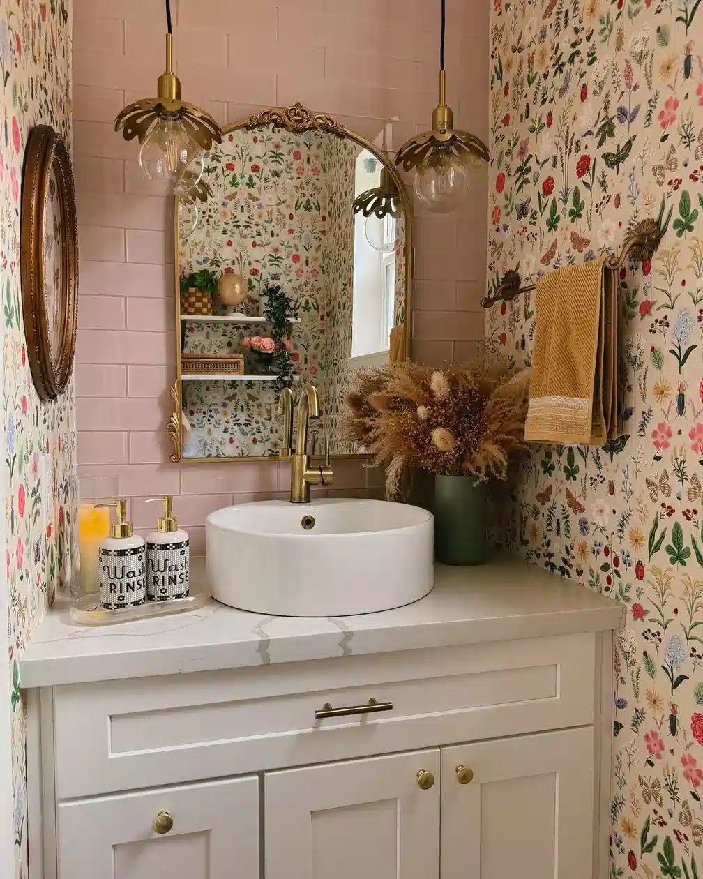Bathroom with tiny floral and insect wallpaper, brass fixtures, flower-shaped pendant lights, and pale vanity