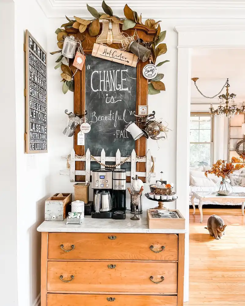 Vintage fall coffee station with oversized chalkboard, leafy garland, metal mugs, wood cabinet, and coffee maker