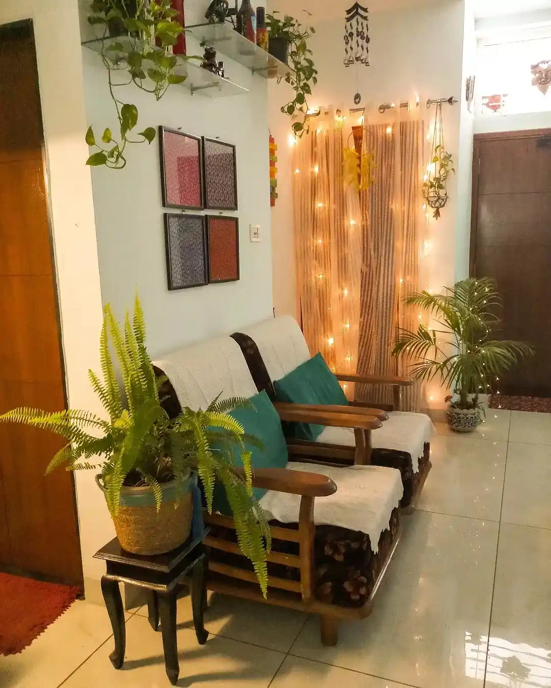 Cozy seating area framed by large green plants, wooden chairs, teal cushions, and warm string lights